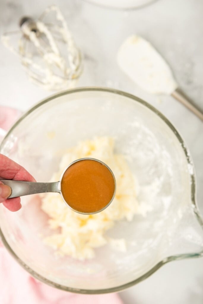 Caramel being added to caramel frosting in stand mixer bowl