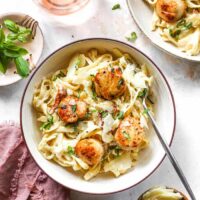 Two bowls of roasted garlic in a creamy pasta sauce with scallops against white background