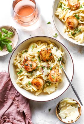 Two bowls of roasted garlic in a creamy pasta sauce with scallops against white background