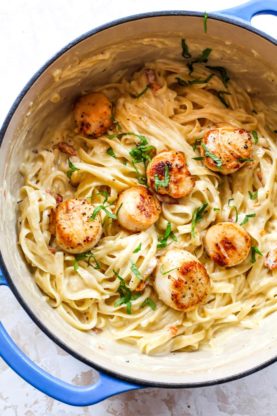 A large pot of pasta with garlic sauce and scallops before serving on plates