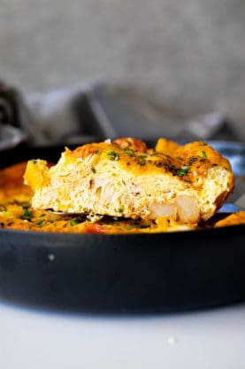 A slice of baked frittata coming out of a cast iron skillet