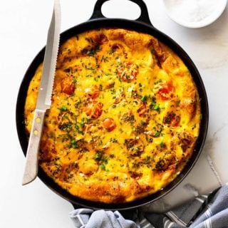 Perfectly baked frittata with tomatoes, potatoes and chicken fresh out of the oven against white background with gray towel