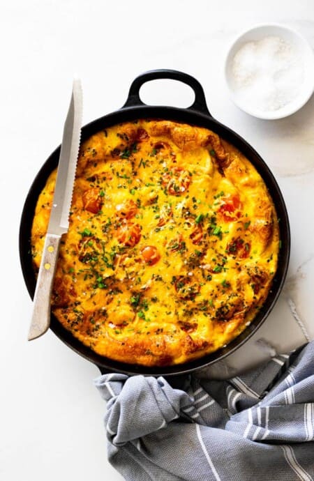 Perfectly baked frittata with tomatoes, potatoes and chicken fresh out of the oven against white background with gray towel