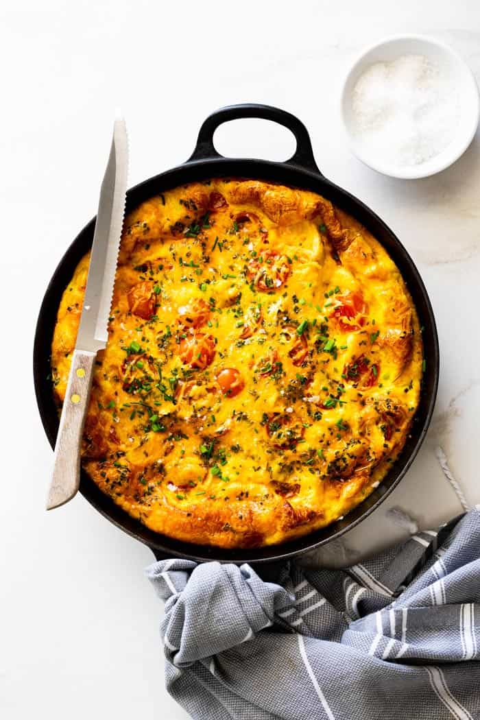 Perfectly baked frittata with tomatoes, potatoes and chicken fresh out of the oven against white background with gray towel