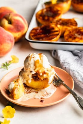 Grilled peaches with vanilla ice cream melting over it and caramel sauce melting over it