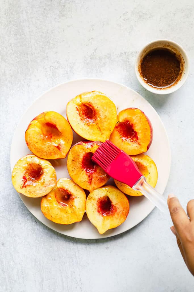 Peach halves being brushed with brown sugar glaze on a white plate