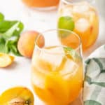 Peach sweet tea in two glasses surrounded by a pitcher, fresh peaches and mint