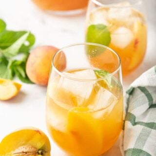 Peach sweet tea in two glasses surrounded by a pitcher, fresh peaches and mint