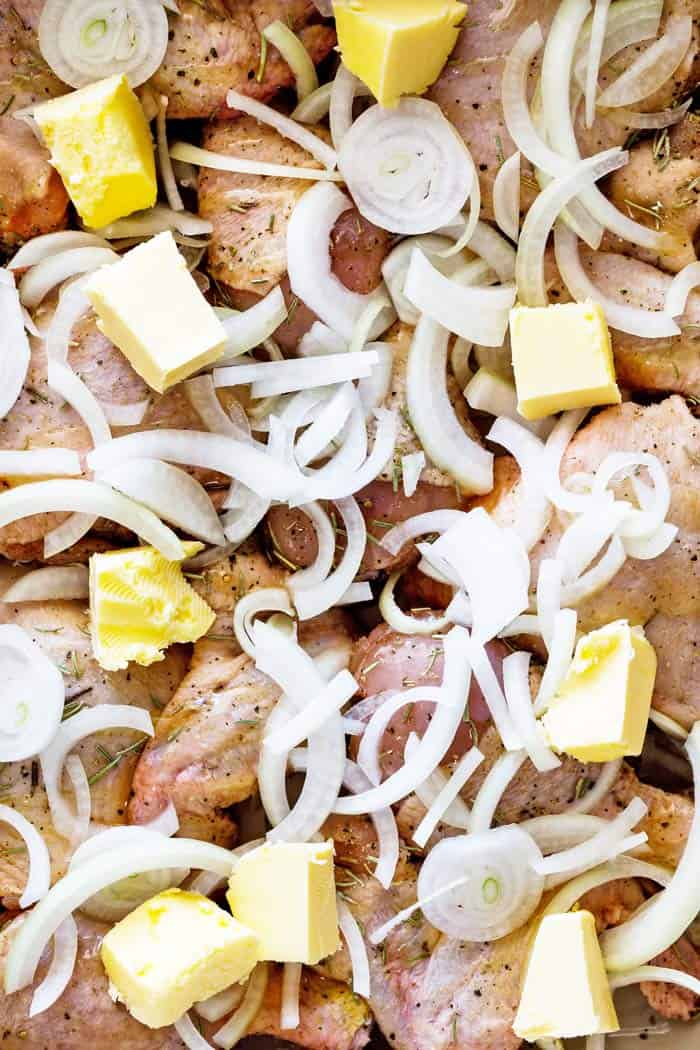 A close up of fresh raw chicken, sliced onions and butter pats before the chicken goes in the oven to bake