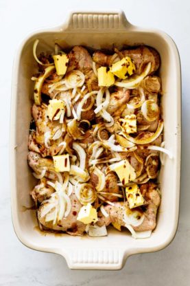 Raw chicken, onion slices, butter pats and maple syrup drizzled over chicken before baking