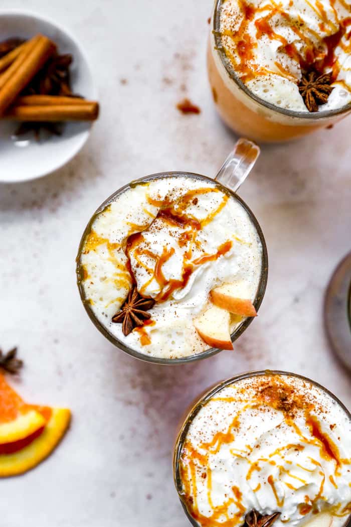 An overhead of three mugs of apple cider with cinnamon sticks and orange slices