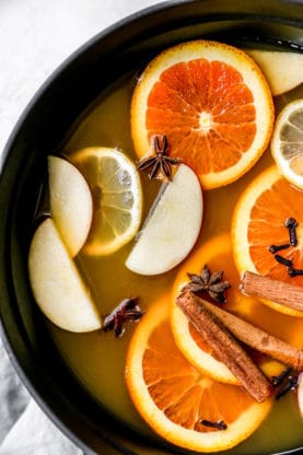 An overhead of a crockpot filled with apple cider, oranges, apples, lemons, cinnamon and nutmeg