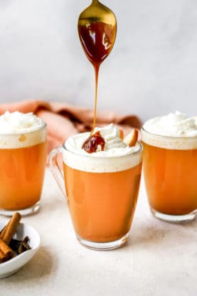 Cider in three mugs with caramel sauce drizzled on top