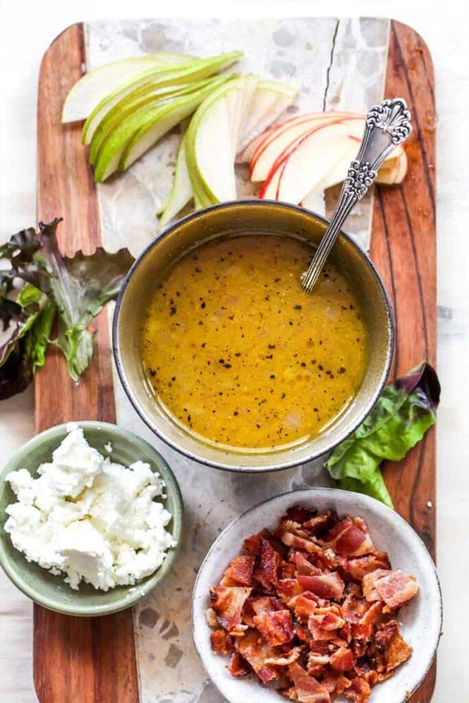 Apple cider dressing, feta cheese, bacon, fresh greens and apple and pear slices arranged in bowls to make a fall salad