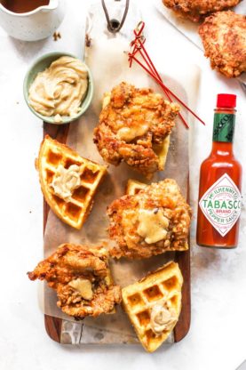 Fried chicken pieces arranged on top of waffle pieces with maple butter next to hot sauce