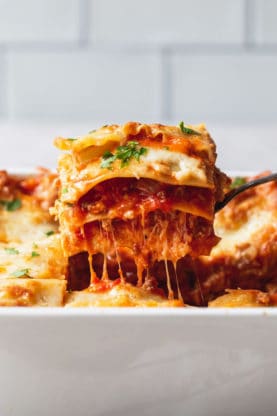 A slice of classic lasagna being lifted out of the pan with a cheese pull