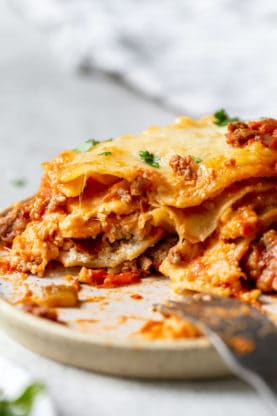 A large plate of a slice of lasagna with a fork being eaten