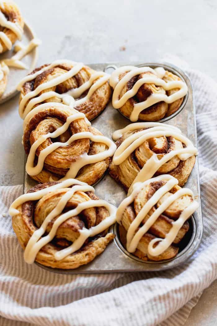 Honey butter cinnamon roll biscuits in a tin topped with cream cheese icing in a drizzle design against gray background