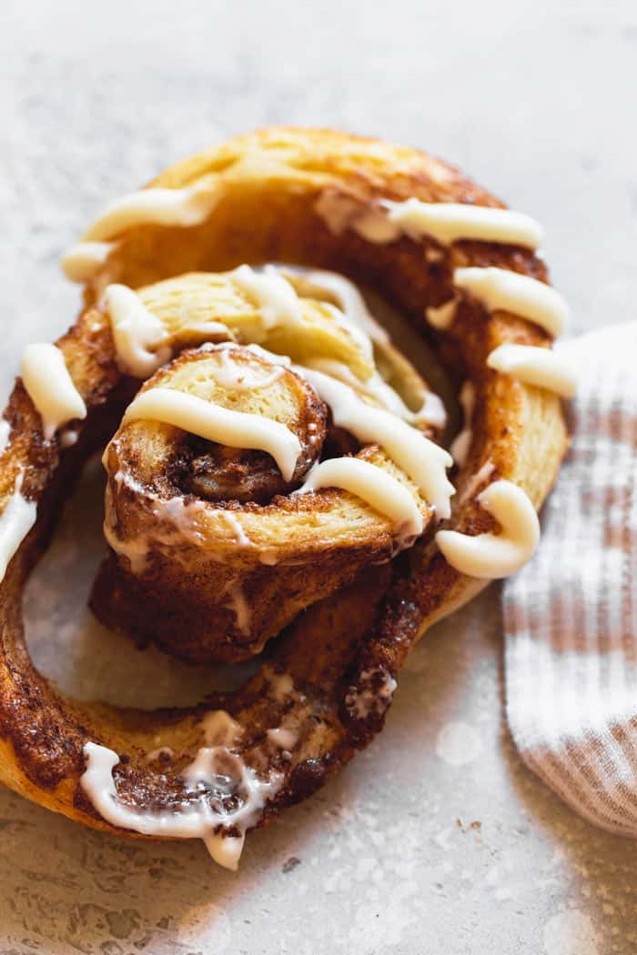 A close up of cinnamon biscuit with cream cheese frosting being pulled apart to show flakiness