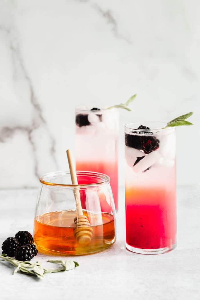 Two glasses of Honey Refresher next to a glass of honey and blackberries