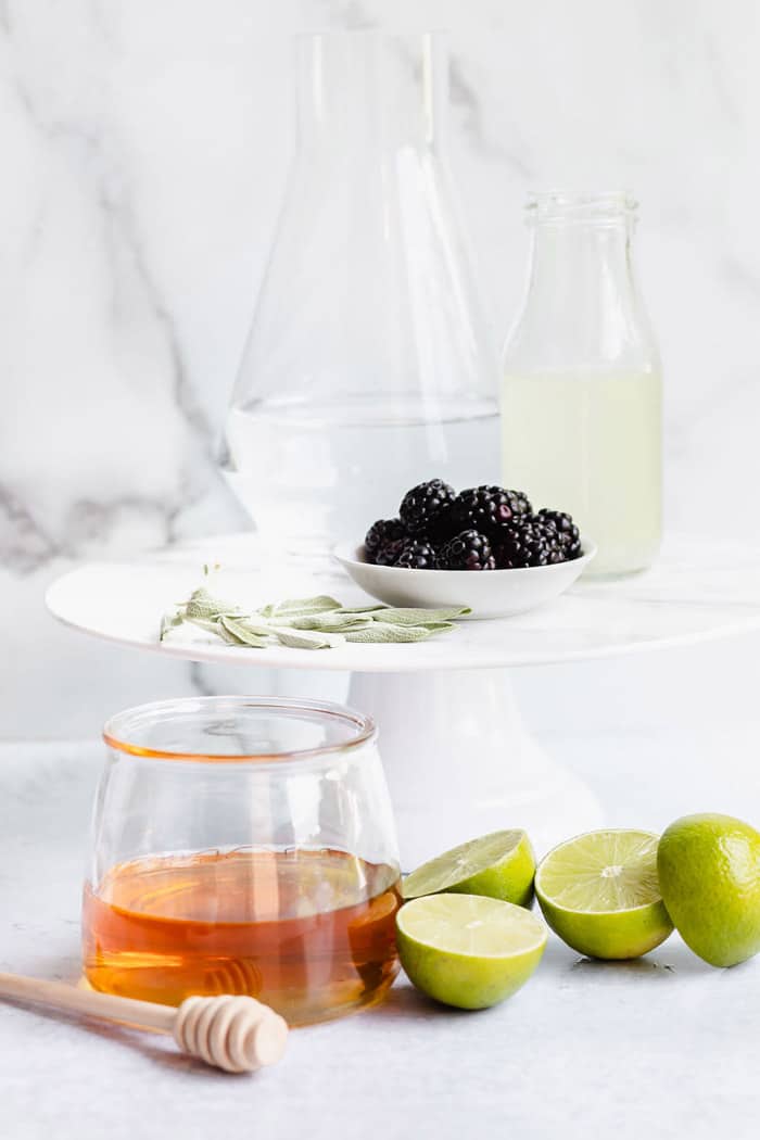 Ingredients to make refresher with slices of lime, honey and blackberries and sage leaves