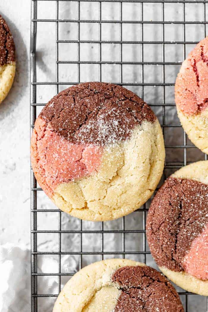 A close up of sugar cookies with strawberry, vanilla and chocolate flavor cooling on a wire rack