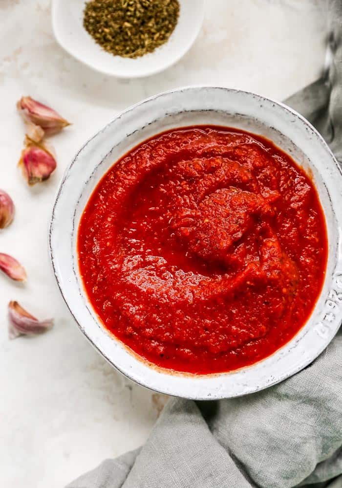 A large bowl of homemade pizza sauce with garlic nearby