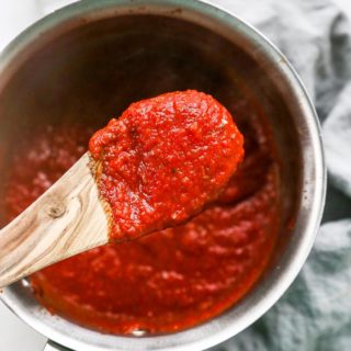 A wooden spoon removing homemade pizza sauce from a pot