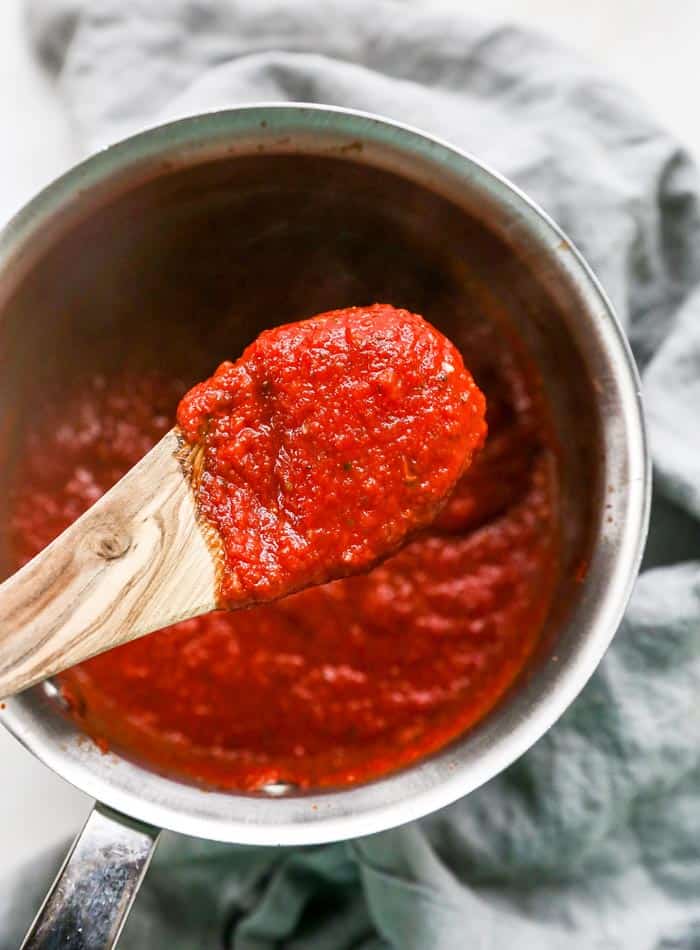 A wooden spoon removing homemade pizza sauce from a pot