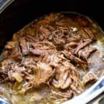 A crockpot filled with shredded Italian beef swimming in a peppery gravy