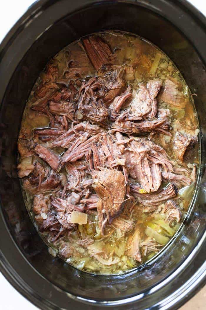 A large slow cooker filled with italian beef after being cooked for the entire day