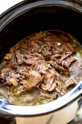 A crockpot filled with shredded Italian beef swimming in a peppery gravy