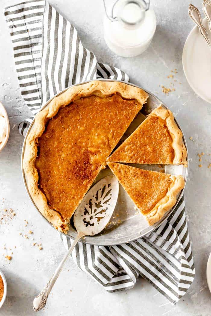 A whole egg pie recipe with slices missing against a striped napkin against a white background