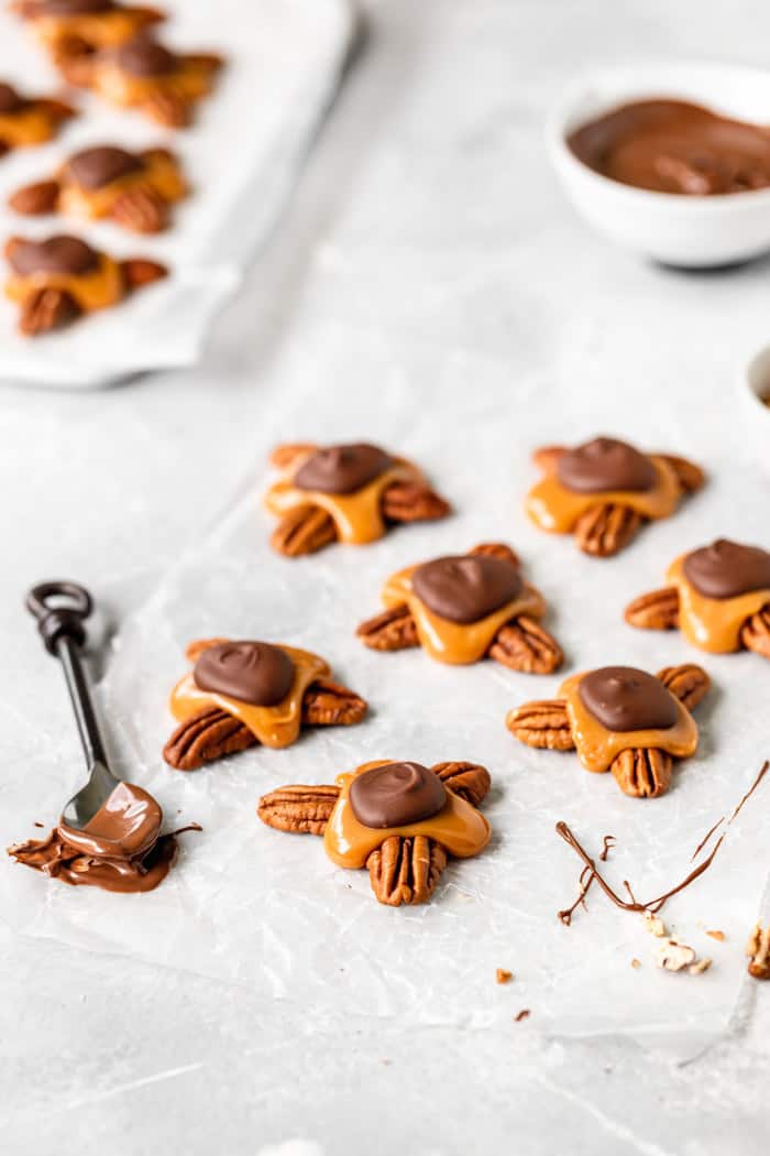 A white background with candies made with chocolate, caramel and pecans with a spoon dipped in chocolate