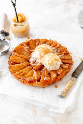 A classic french apple tarte ready to serve with ice cream and cream sauce against white background