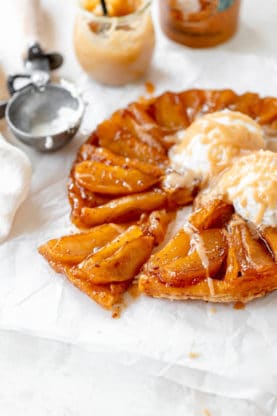 A slice of french apple tarte tatin being pulled out with ice cream and cream sauce melting on top