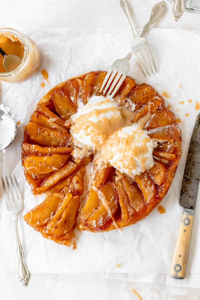 Apple Tarte Tatin with vanilla ice cream and cream sauce melting on top with a rusty knife and cream sauce nearby
