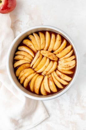 Apple slices arranged on caramel in a baking pan