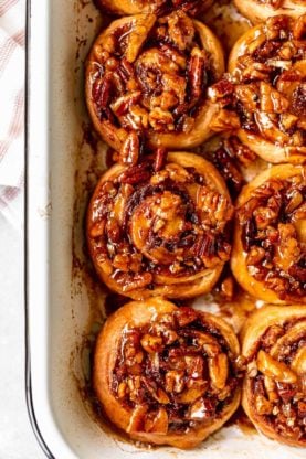 Pecan sticky buns in a white casserole dish after being baked and covered in a pecan glaze