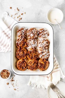 Pecan cinnamon rolls against a white background with a bowl of pecans nearby