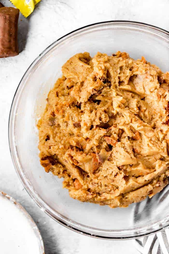 A clear bowl of cookie dough with mixed in butterfinger candy