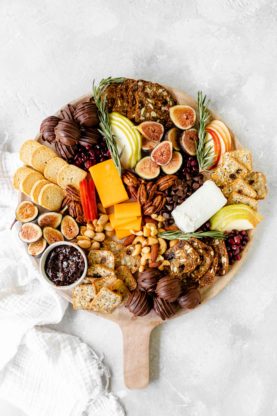 A dessert charcuterie board filled with fruit, chocolate and more against a white background