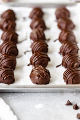 Chocolate truffles lined up on a parchment lined baking sheet ready to chill