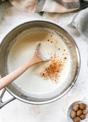 An eggnog in a pot with spices being stirred with a wooden spoon