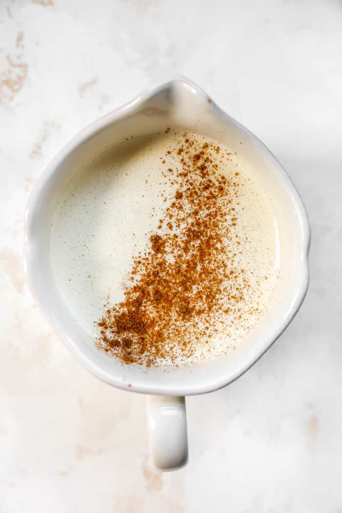 A glass of eggnog with nutmeg sprinkled on top in a white pot