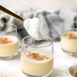 A glass of eggnog being topped with whipped meringue