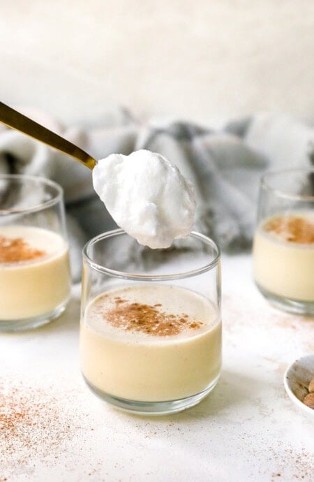 A glass of eggnog being topped with whipped meringue