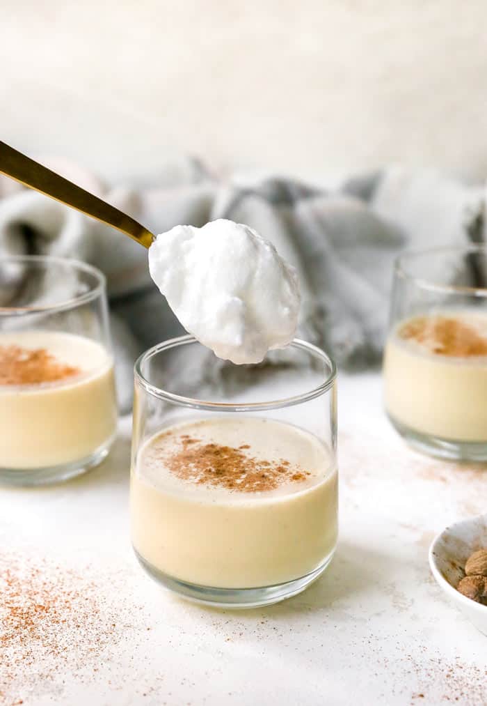 A glass of eggnog being topped with whipped meringue