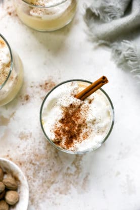 A glass of eggnog with meringue and spices and cinnamon stick