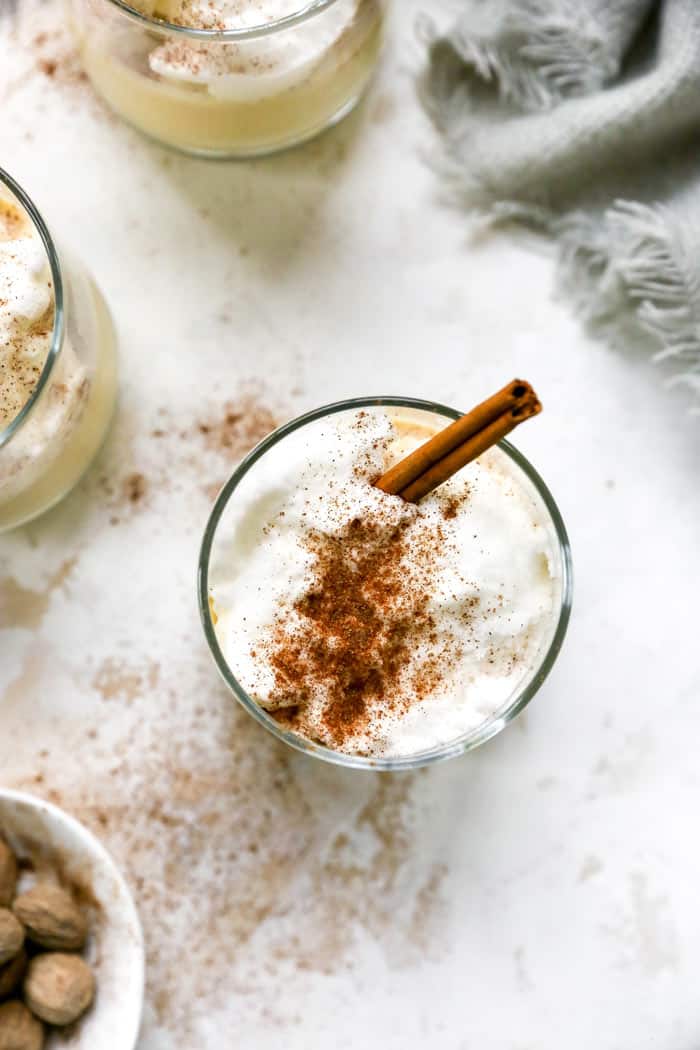 A glass of eggnog with meringue and spices and cinnamon stick